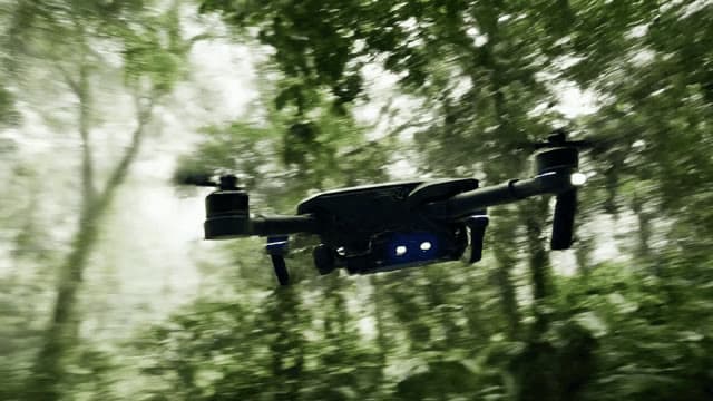 A sleek drone navigates through a dense rainforest, its sensors scanning vibrant flora and fauna. The camera follows closely, capturing the intricate details and dynamic motion beneath the canopy.